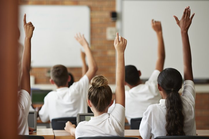 children with hands up in classroom - GETTY IMAGE