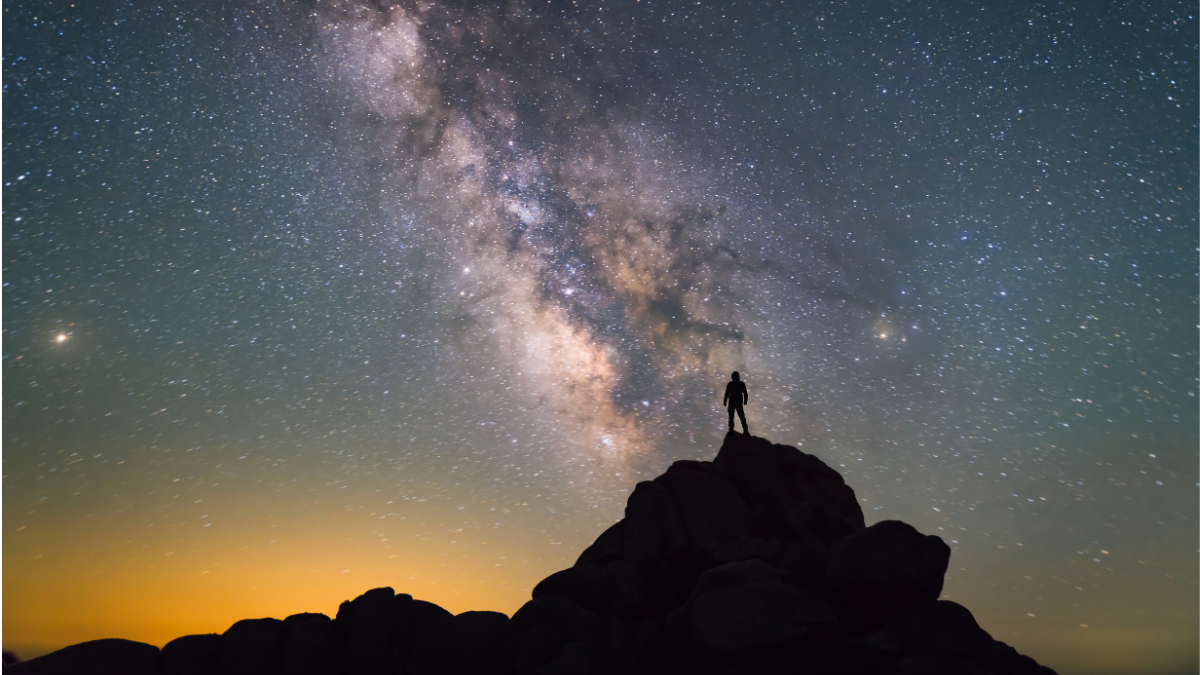 silhouette of a man standing on a rock against the milky way in the sky