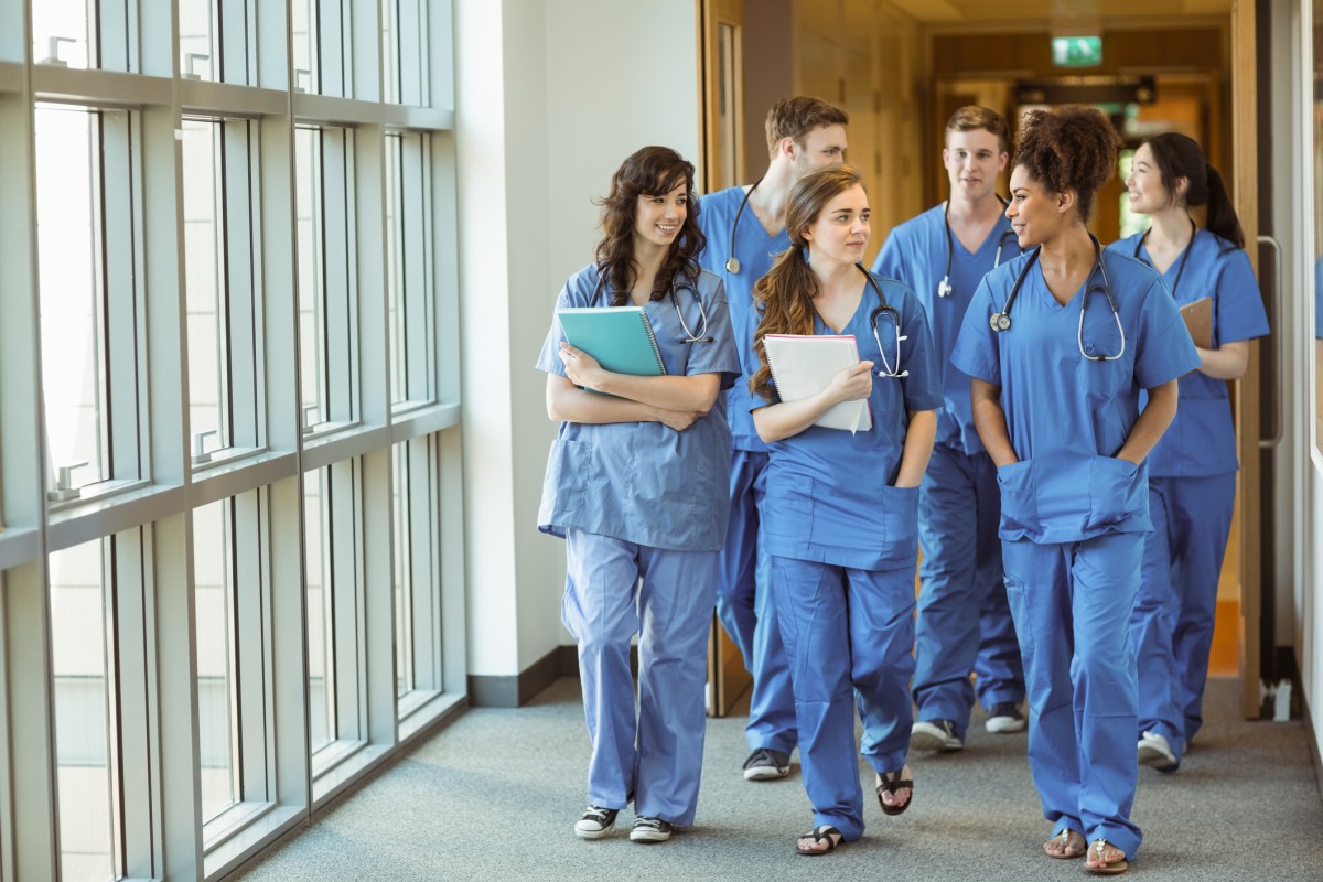 Group of medical students in scrubs walking through open doors on a hospital corridor