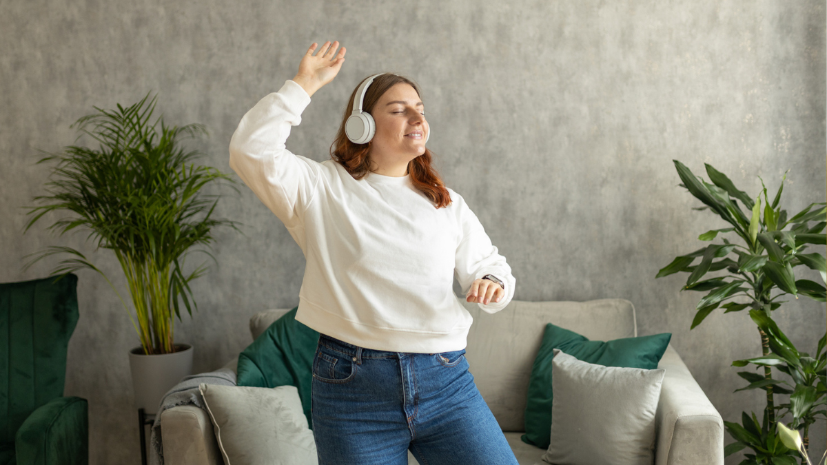woman dancing while listening to wireless headphones in her living room