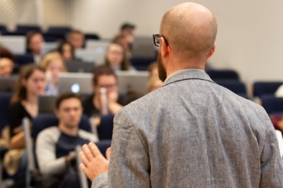 Lecturer speaks to students a busy lecture hall