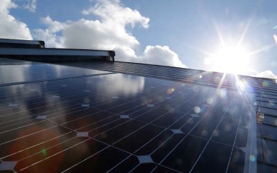 The sun glints off some solar panels in front of a blue sky studded with fluffy clouds