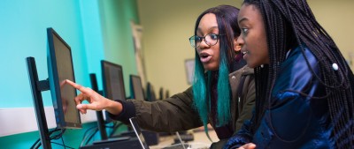 Two students, head and shoulders, pointing at computer screen