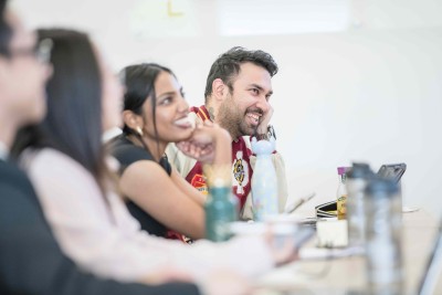 MBA students sitting at a desk smiling at unseen speaker