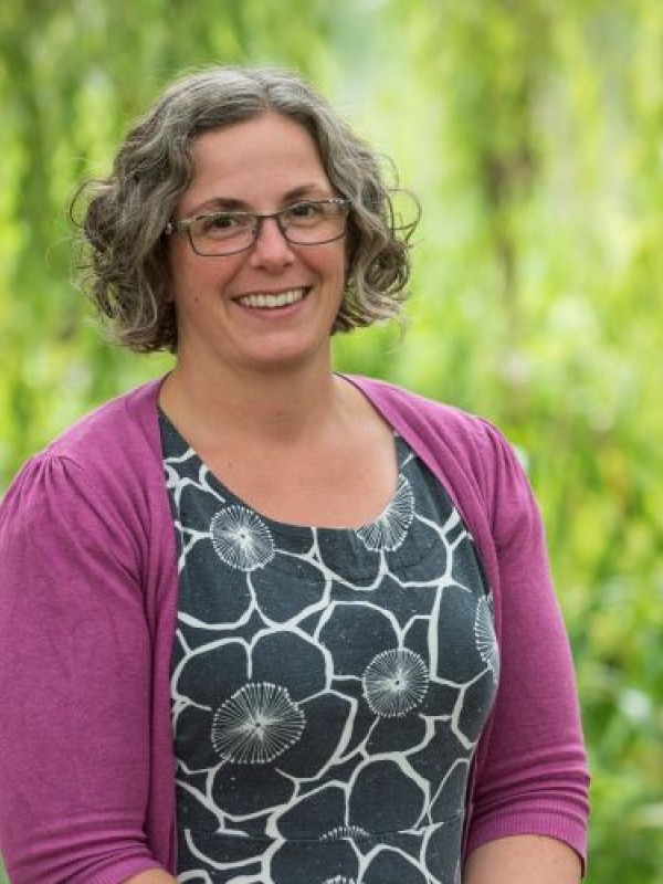 Woman standing with short curly brown and grey hair, wearing glasses