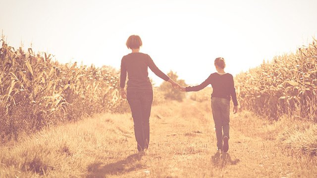 A mother and daughter walking hand in hand through a golden field