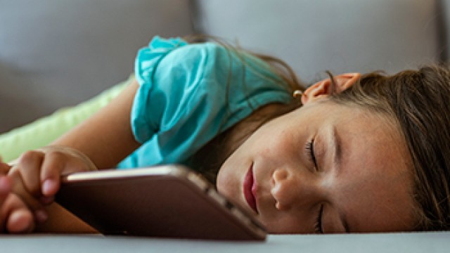 A young girl is asleep in front of a mobile phone