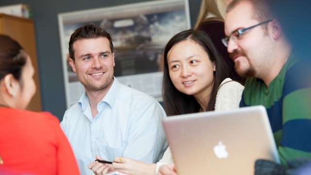 Four Surrey Executive MBA students sitting around a laptop