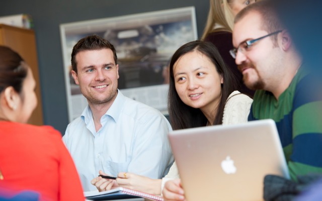 Four Surrey Executive MBA students sitting around a laptop