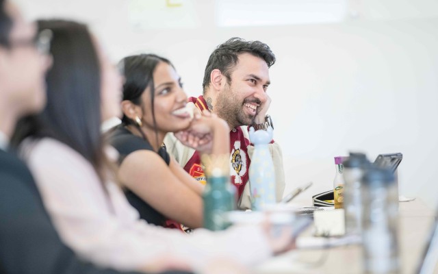 MBA students sitting at a desk smiling at unseen speaker