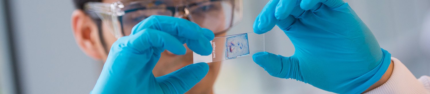 A student wearing blue gloves and googles is holding up a slide