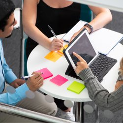 Group of students sat around a table writing notes and using an iPad