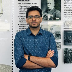 Udbhav wears glasses and a blue shirt, he is looking at the camera with his arms crossed.