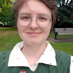 A smiling person with octagonal grey glasses and light brown hair