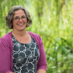 Woman standing with short curly brown and grey hair, wearing glasses