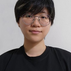 A photo of Ren Khaw facing the camera. He is in a black shirt against a light grey background.