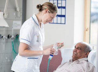 Student nurse putting breathing mask on elderly patient laying in a bed