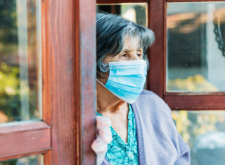 Woman wearing face mask looks out of a care home window