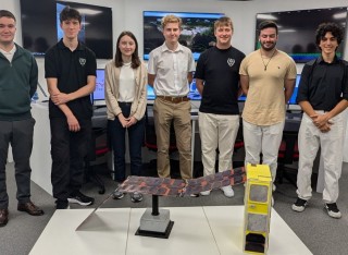 Some of the Surrey students involved with making the Jovian-1 satellite stand in the Surrey Space Centre's Ground Station with a life-sized model of the satellite in front of them