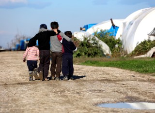 A group of refugee children with their arms around each other walking