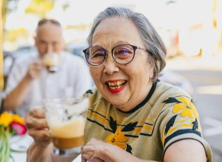 Older lady smiling with a cup of coffee in street cafe