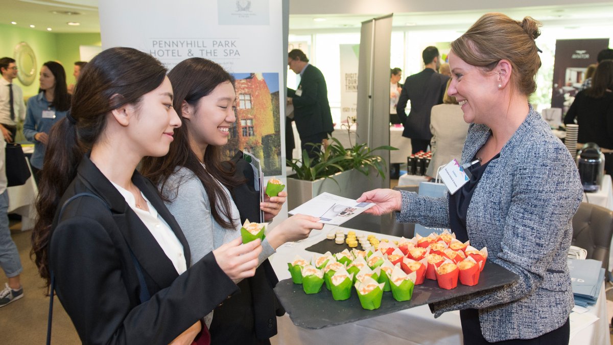 Two female students taking a card from a prospective employer