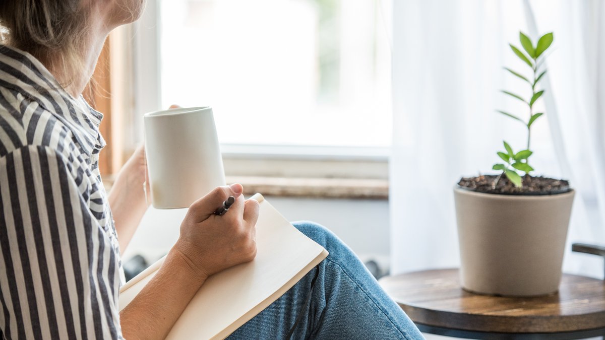 Woman holding a pen and pad in one hand and a mug in the other