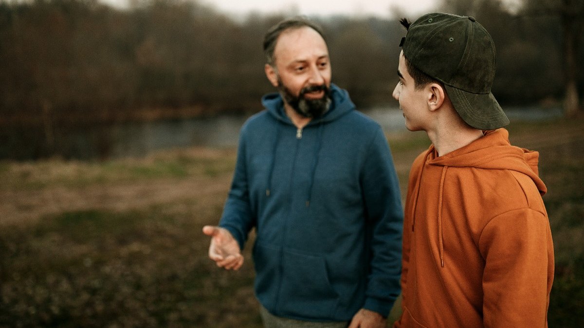 A man and boy talk as they walk through a green space