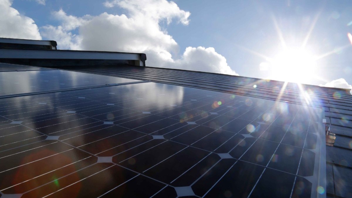 The sun glints off some solar panels in front of a blue sky studded with fluffy clouds