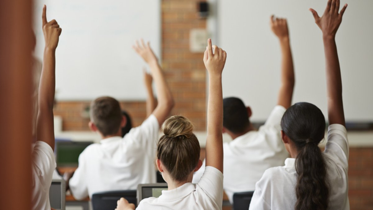 children with hands up in classroom - GETTY IMAGE