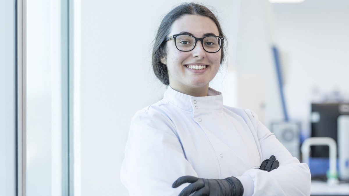 A biosciences student wearing glasses smiles confidently at the camera with her arms crossed.