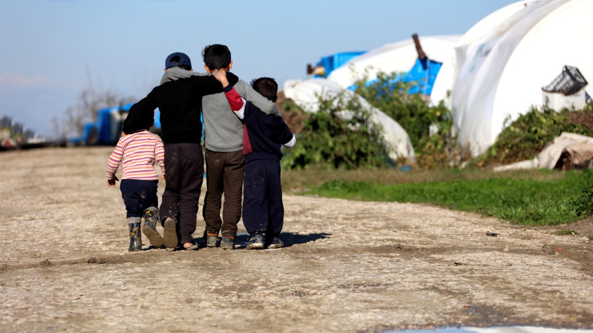 A group of refugee children with their arms around each other walking